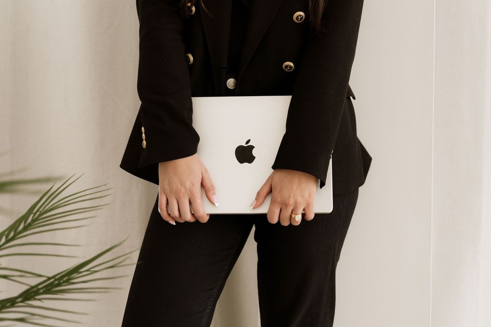 Close-up view of hands holding white MacBook laptop against black business attire.