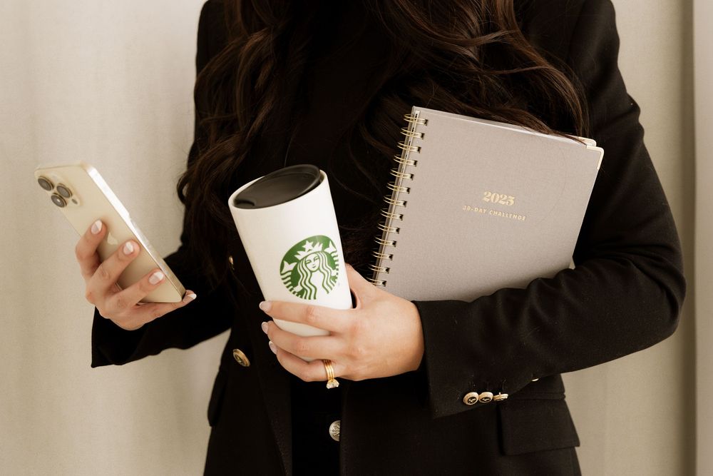 Professional holding Starbucks coffee, notebook and phone while wearing business attire.