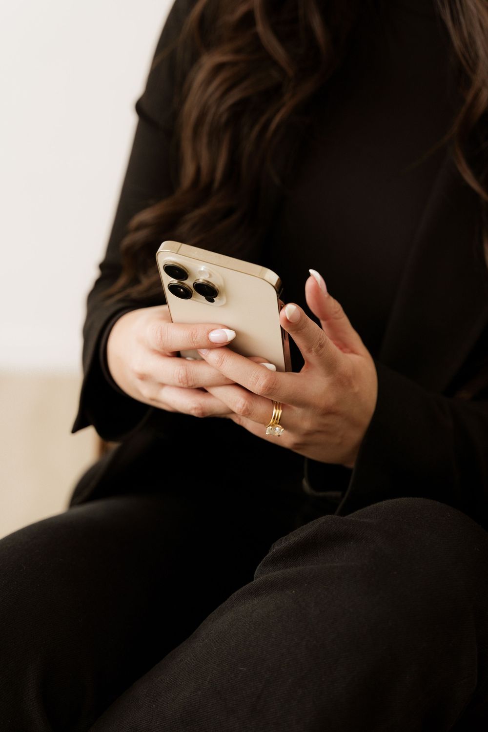 Close up of hands holding iPhone Pro with gold ring in cozy minimal setting.