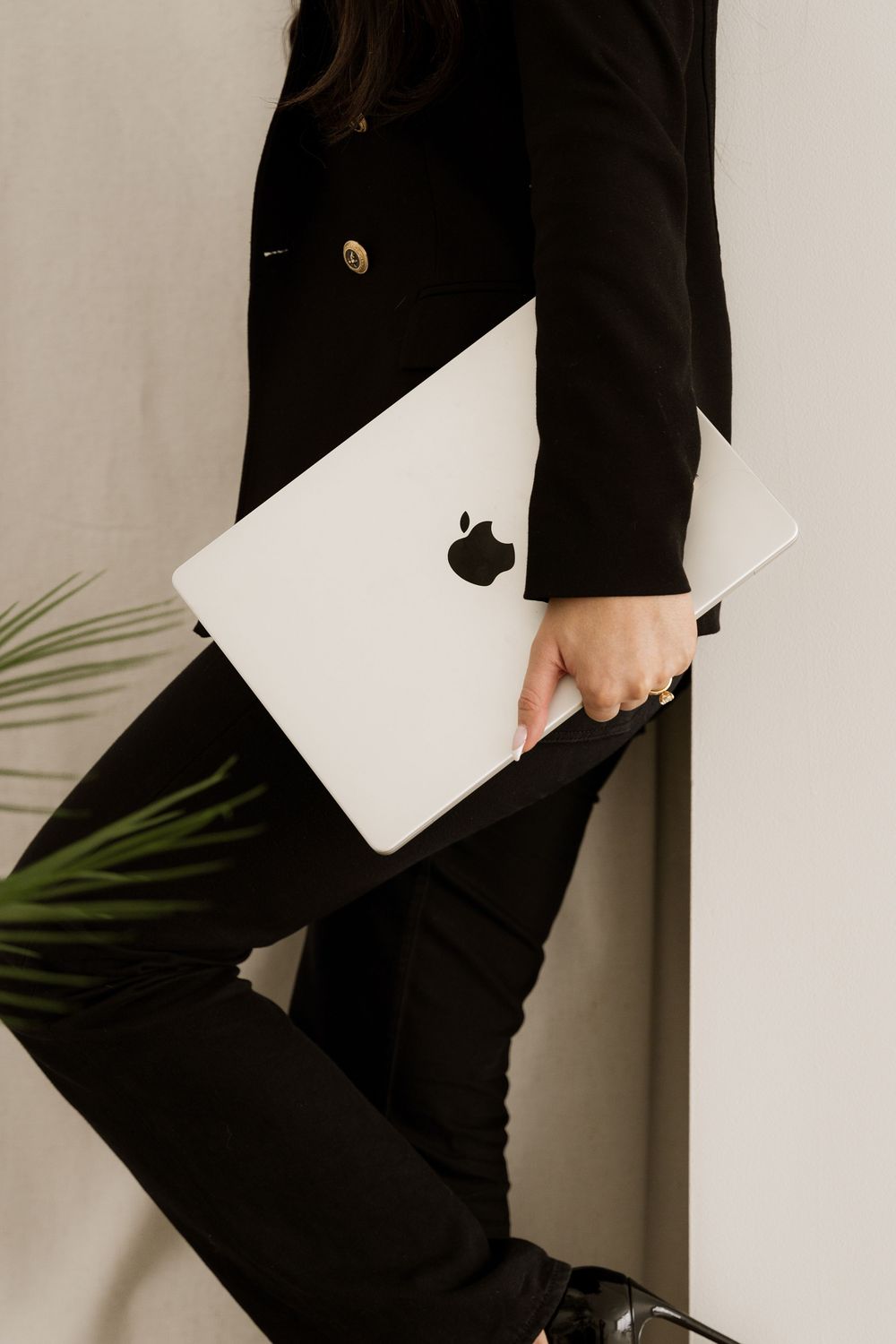 Close up of hand holding white MacBook laptop against black blazer and light background.