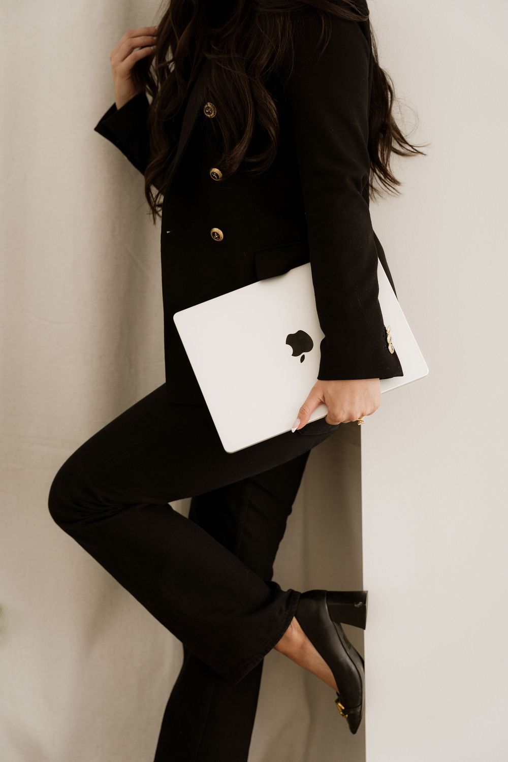 Person in black outfit with MacBook laptop working in minimalist office setting.
