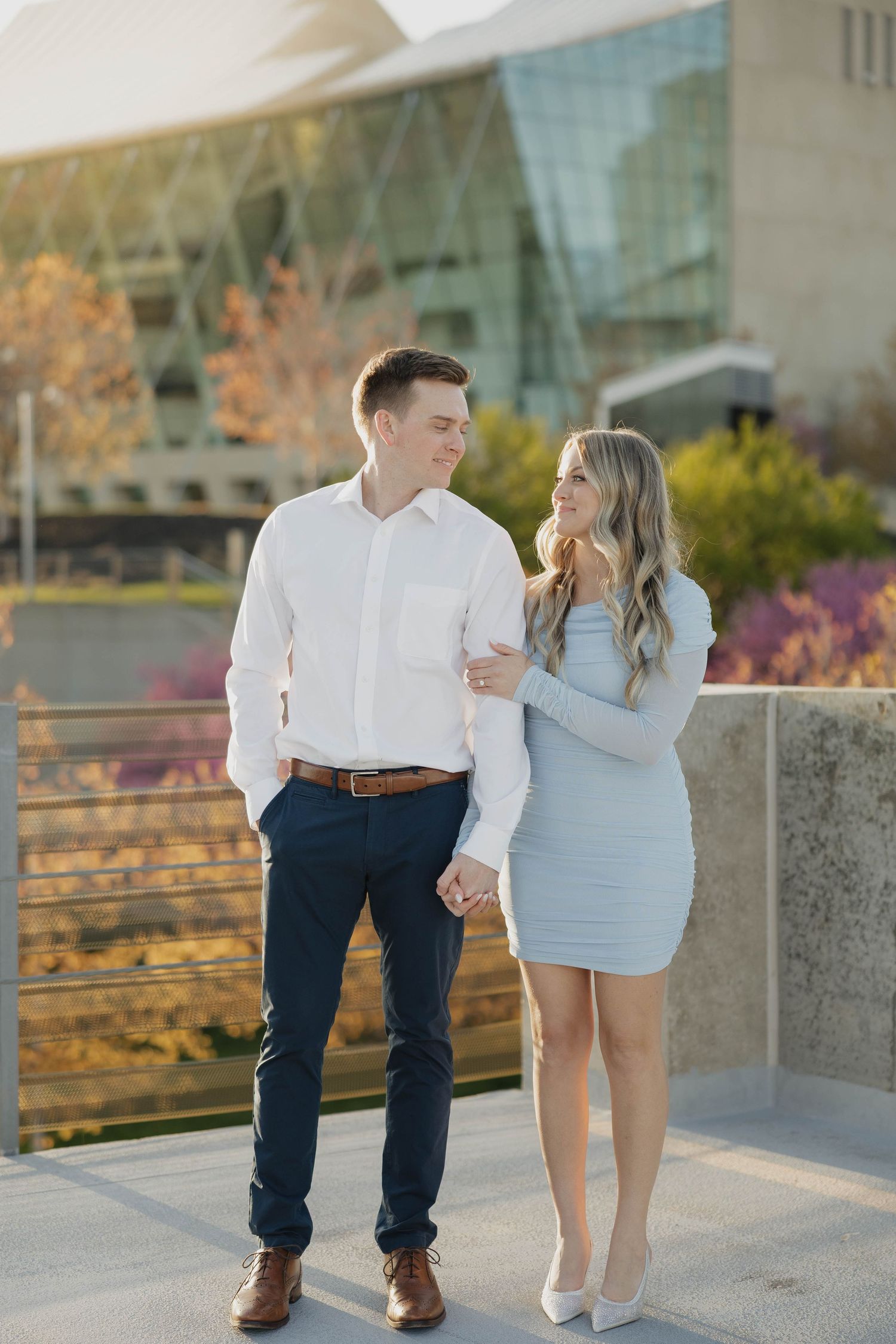 A couple in matching white and blue outfits stand close together on an outdoor terrace during golden hour.