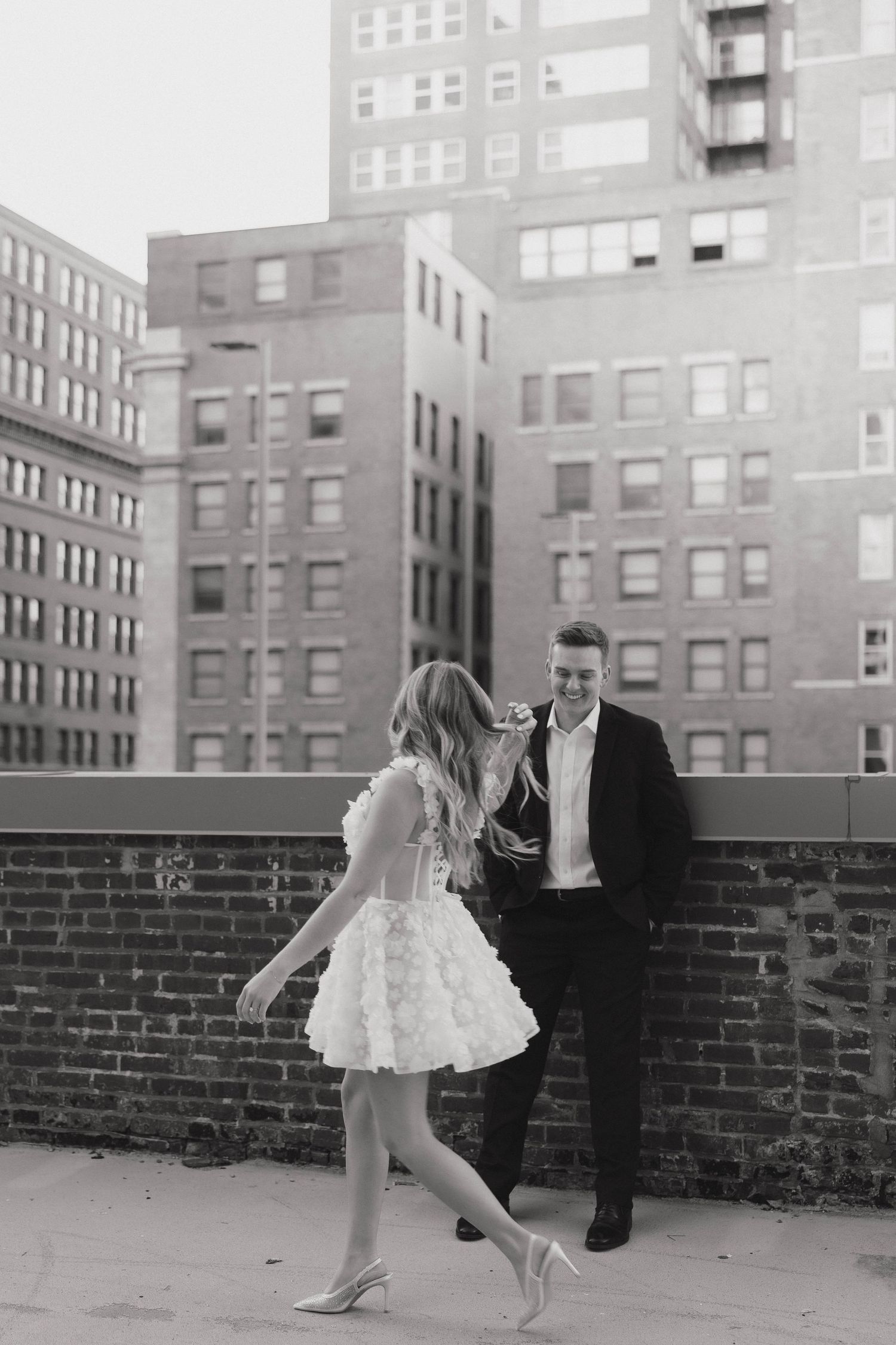A couple sharing a romantic moment on an urban rooftop with brick walls and city buildings in the background.