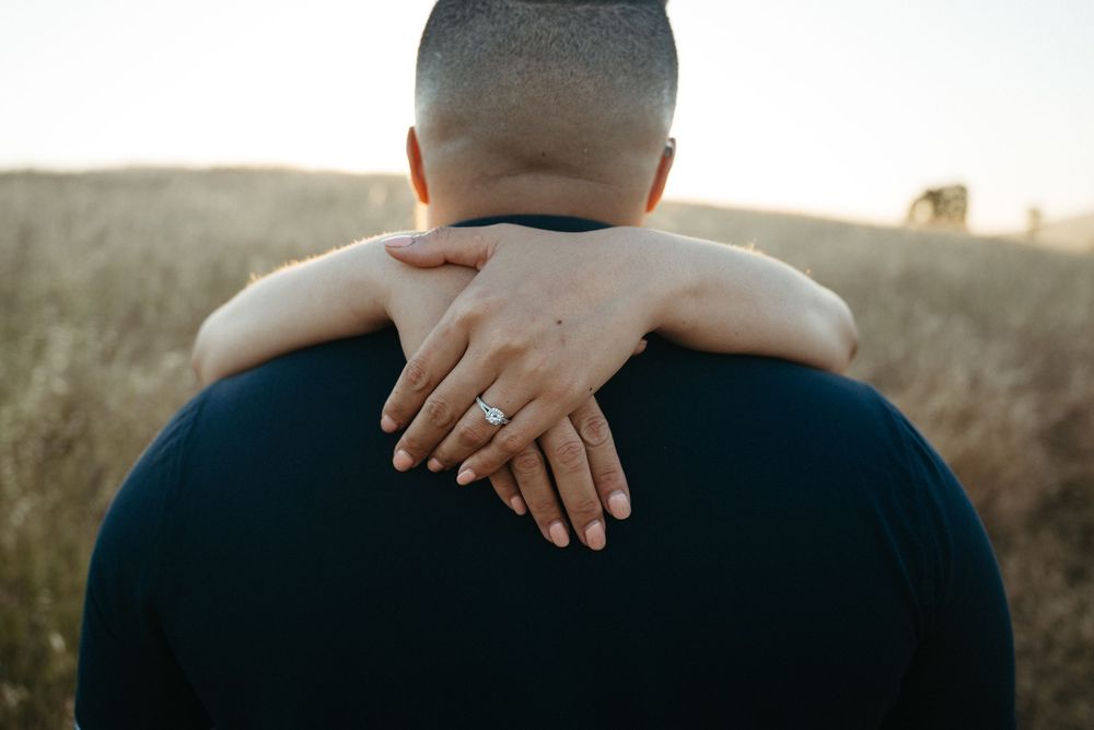 A close-up view of hands embracing around shoulders against a sunlit grassy field background.