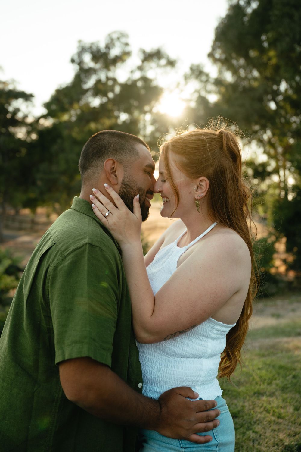 A romantic sunset photoshoot shows a couple embracing in a green outdoor setting.