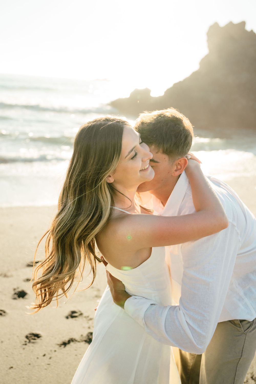 Romantic couple embraces on sandy beach at golden sunset with ocean waves in background.