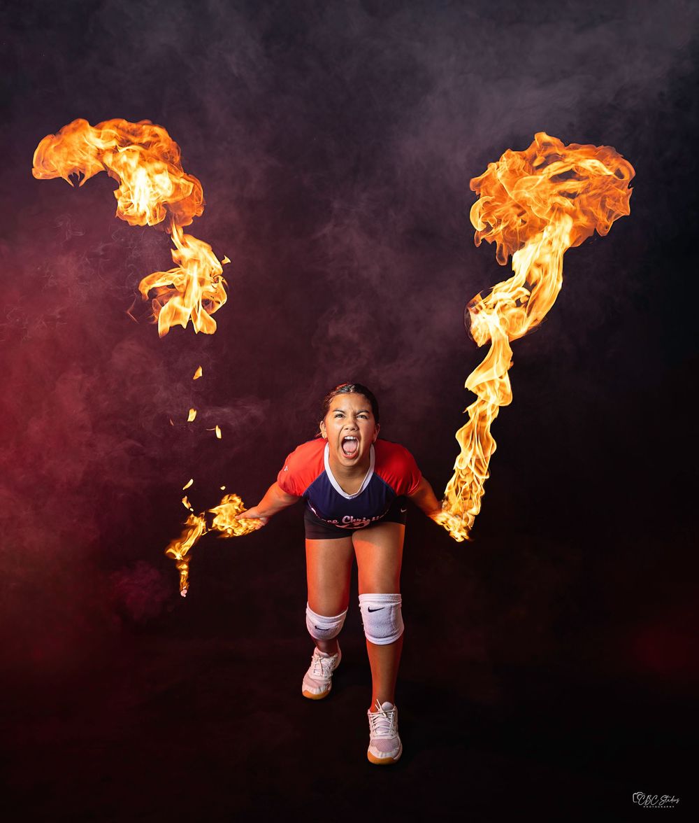 Athlete poses energetically with fire torches in dramatic smoke-filled studio setting.