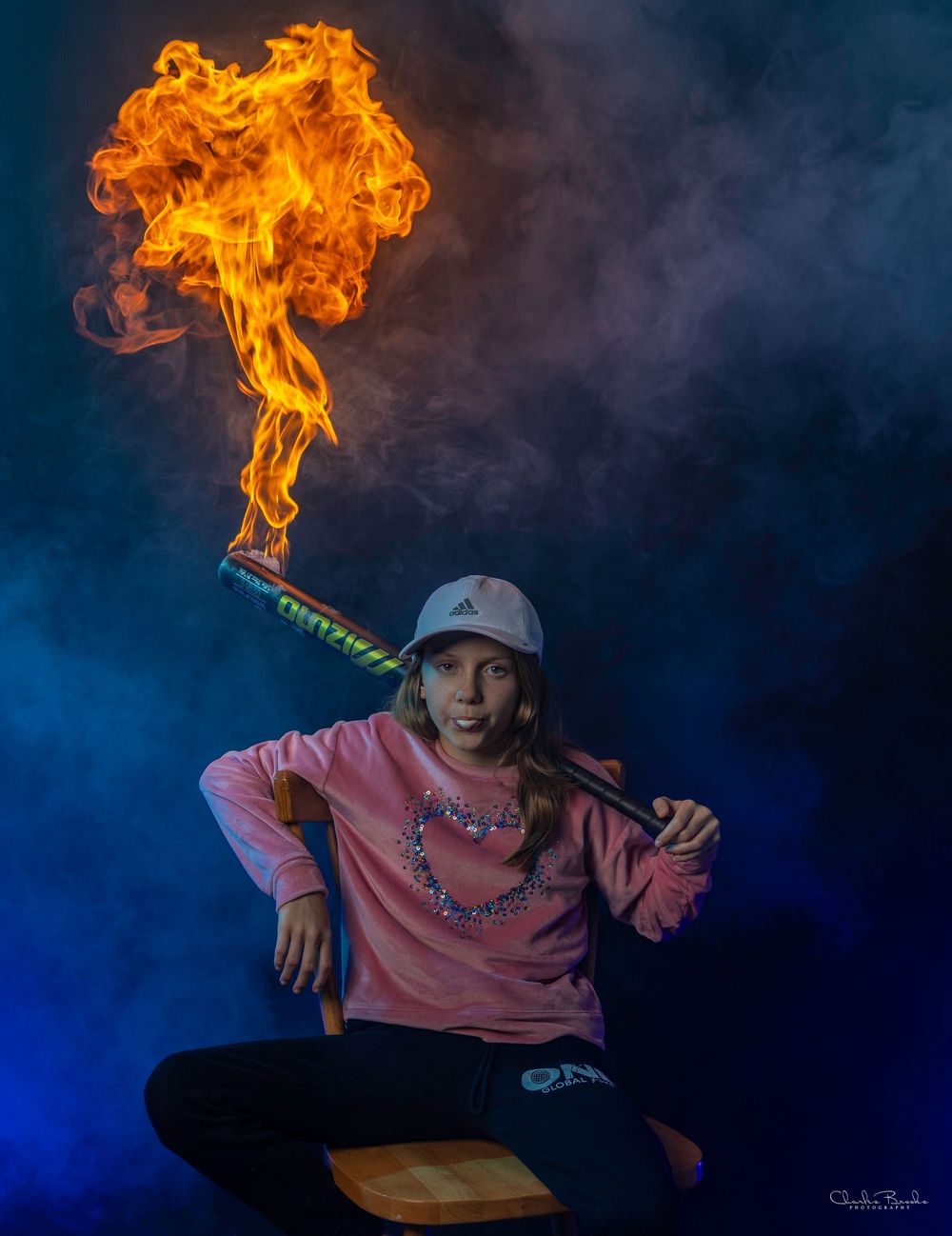 Person in pink sweater poses with flaming stick against blue and black background.