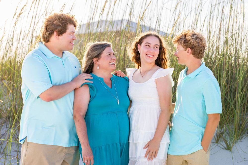 A family shares genuine laughter together while standing in front of tall beach grass on a sunny day.