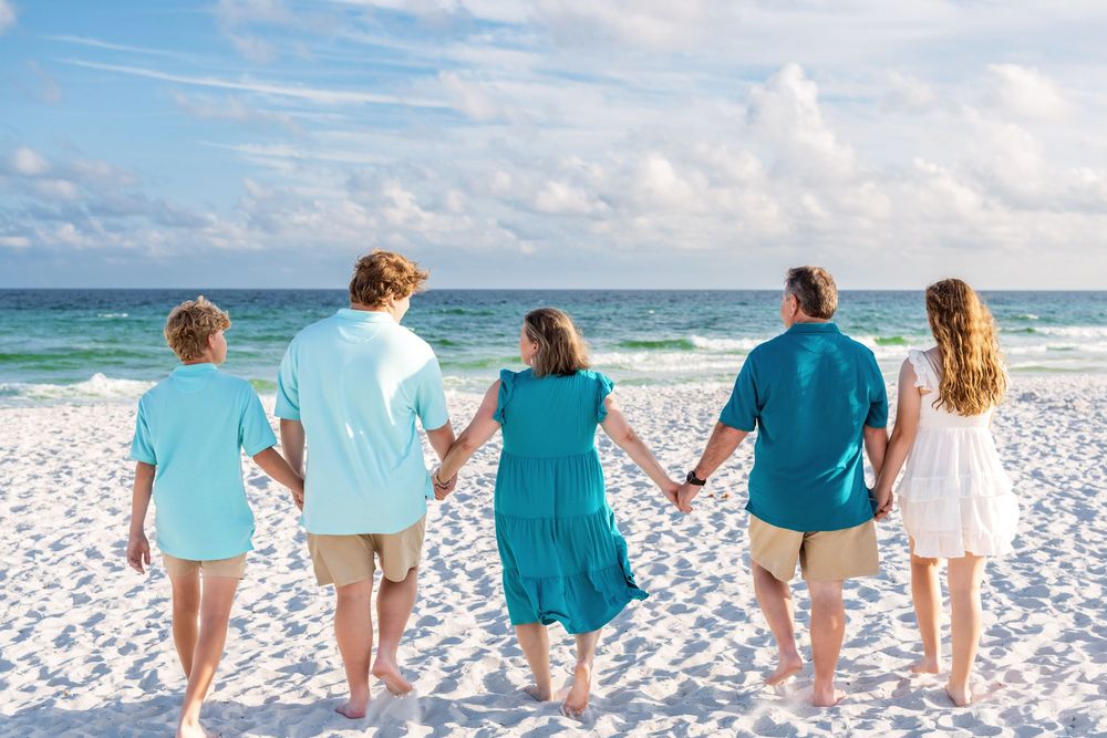 Group walking together hand in hand on a white sandy beach with turquoise ocean and blue sky views.