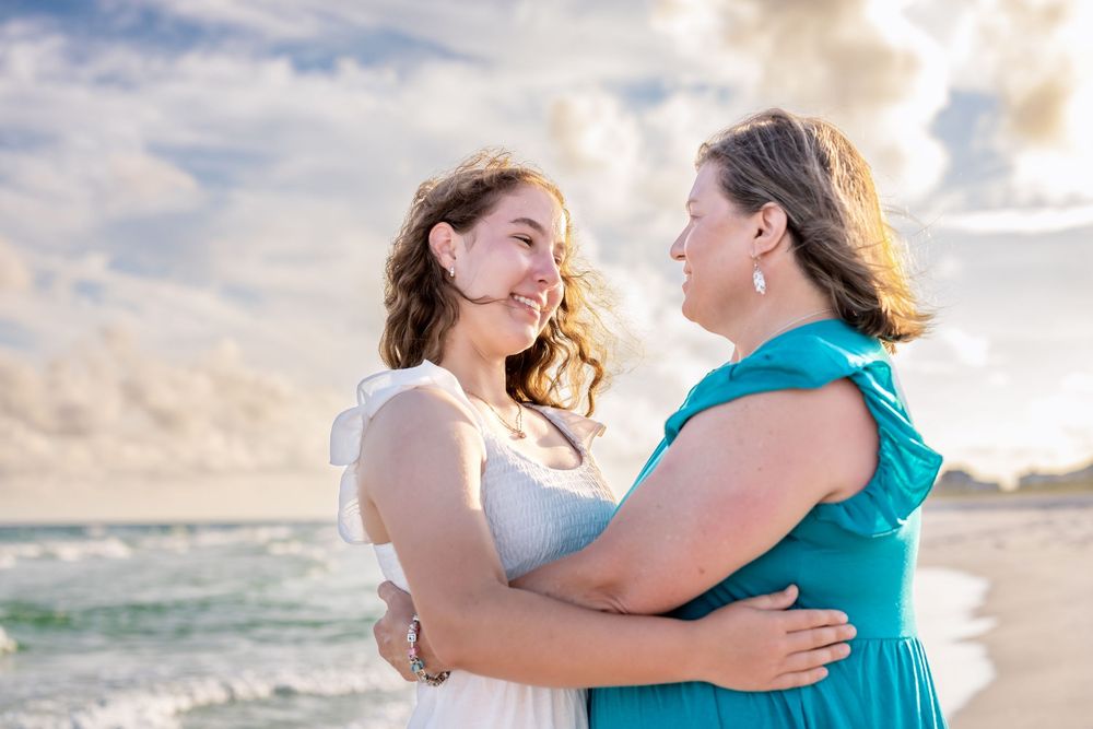 A touching sunset beach photoshoot with two people embracing in coordinated turquoise and white outfits.