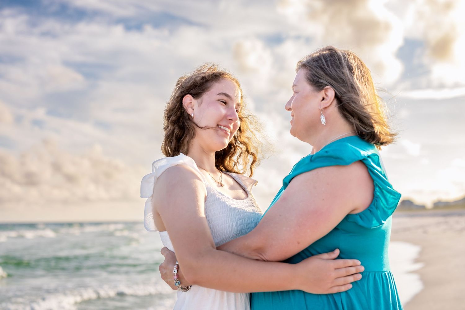 A touching sunset beach photoshoot with two people embracing in coordinated turquoise and white outfits.