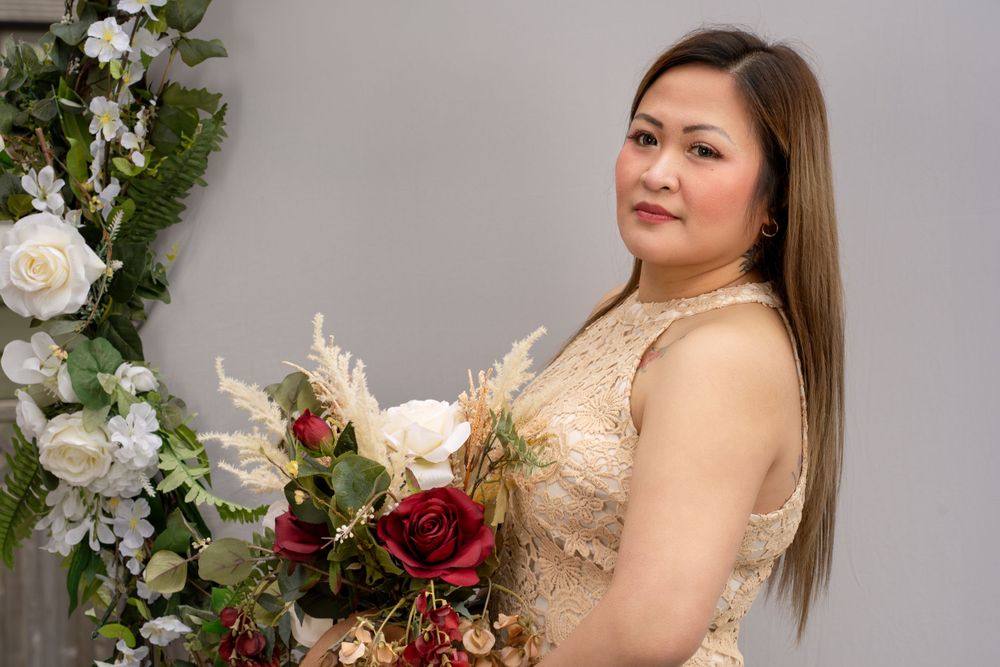 Bridal portrait showcasing a champagne dress and red and white bouquet against grey backdrop.