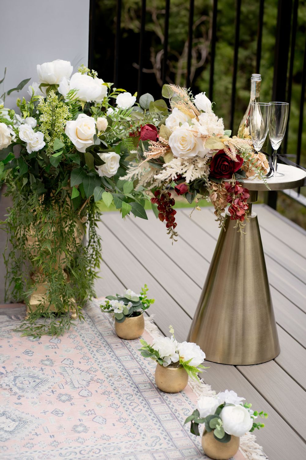 Elegant floral arrangement with white roses and greenery on metallic stand at outdoor wedding reception.