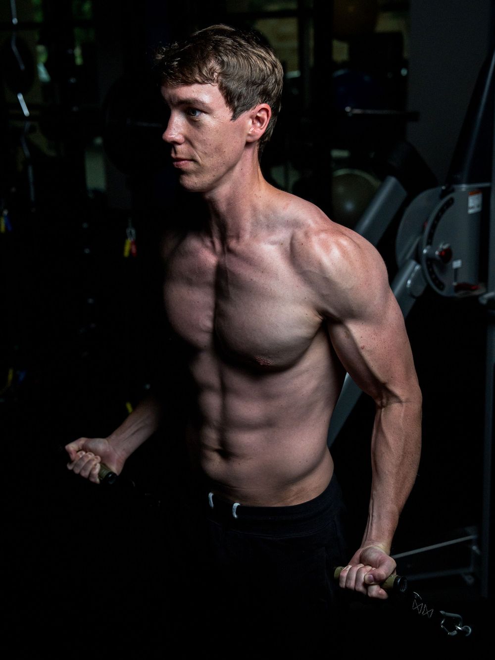 Athletic person performs dips exercise on workout equipment in dimly lit gym showing muscular physique.