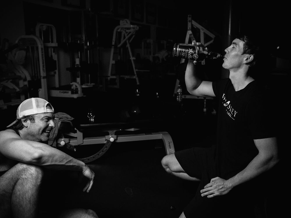 Two people in casual attire sit and drink from water bottles in what appears to be a gym or workout space.