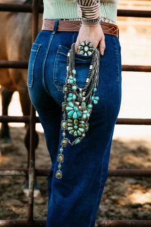 Turquoise statement necklace with floral designs hangs against dark denim jeans in sequential fashion shots.
