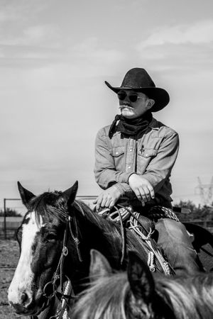 Cowboy wearing a black hat sits mounted on a horse in black and white photography.