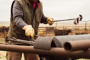 A farrier carefully shapes a red-hot horseshoe on an anvil with professional metalworking tools.