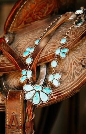 Intricate turquoise stone necklace displayed on ornately tooled brown leather saddle detail.