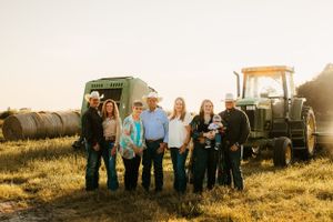 Family group portrait in front of farm equipment during golden hour.