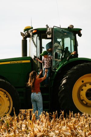 Person reaching up to greet operator in large John Deere tractor during harvest.