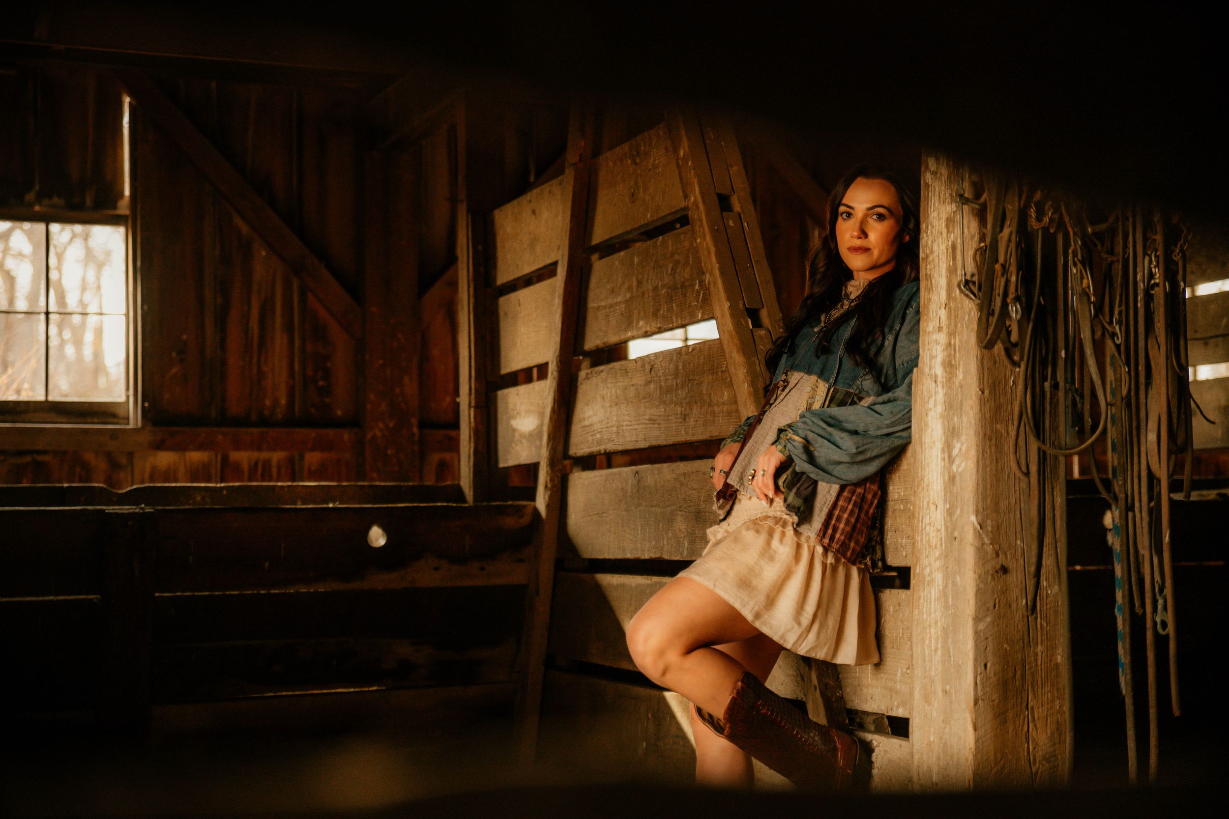 A rustic barn interior lit by natural window light creates a moody atmospheric scene with vintage wooden beams and walls.