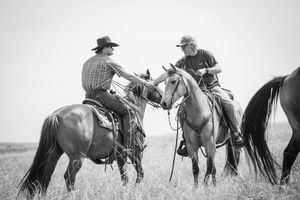 Two cowboys on horseback shaking hands in a field, black and white photography capturing western ranch life.