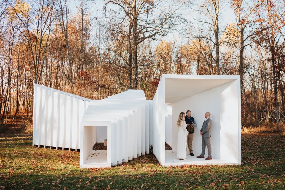 Couple exchanging vows inside a modern white sculptural outdoor wedding ceremony structure.