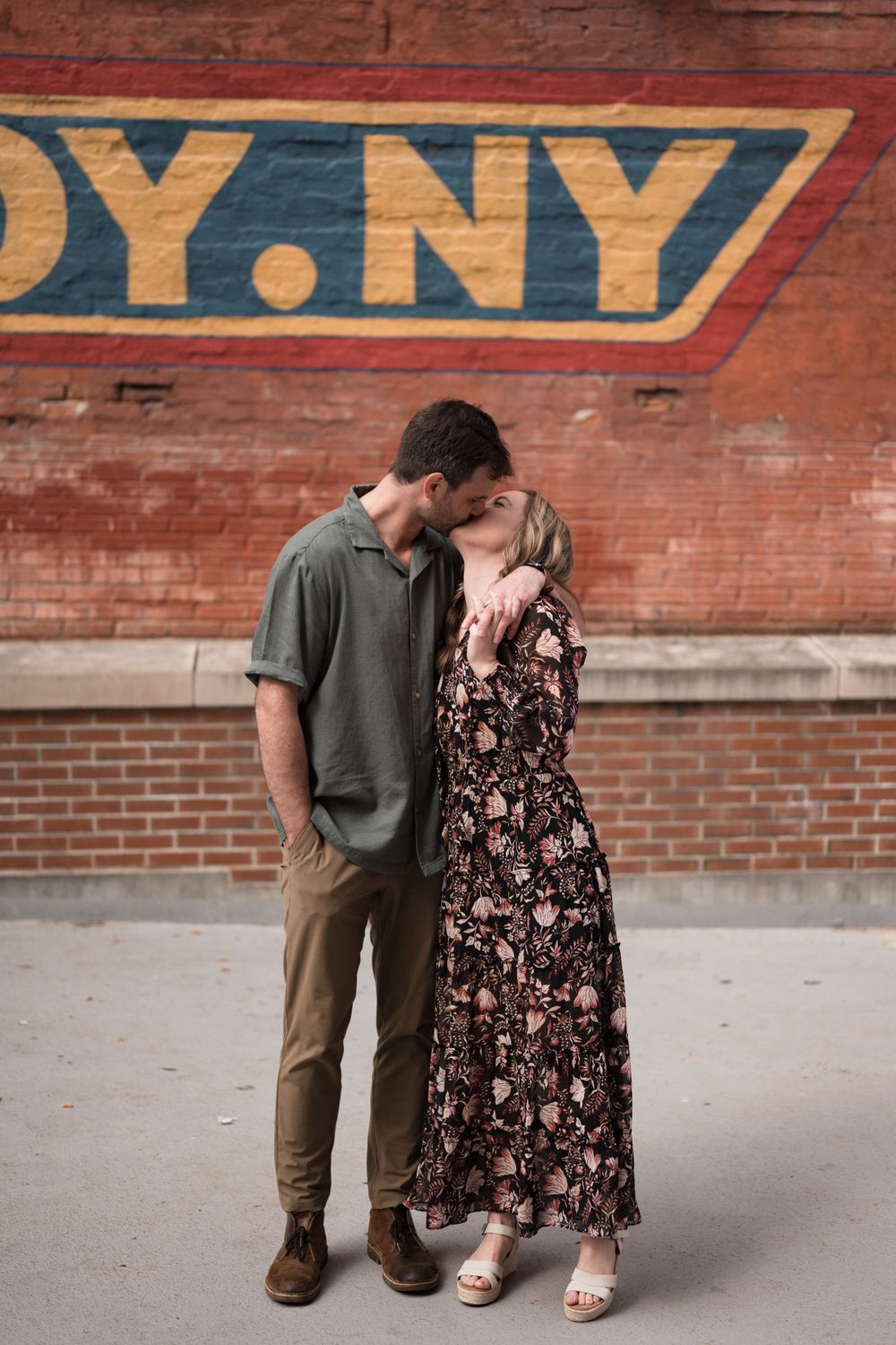 Couple sharing a tender kiss in front of a Troy NY brick wall mural during their engagement session.