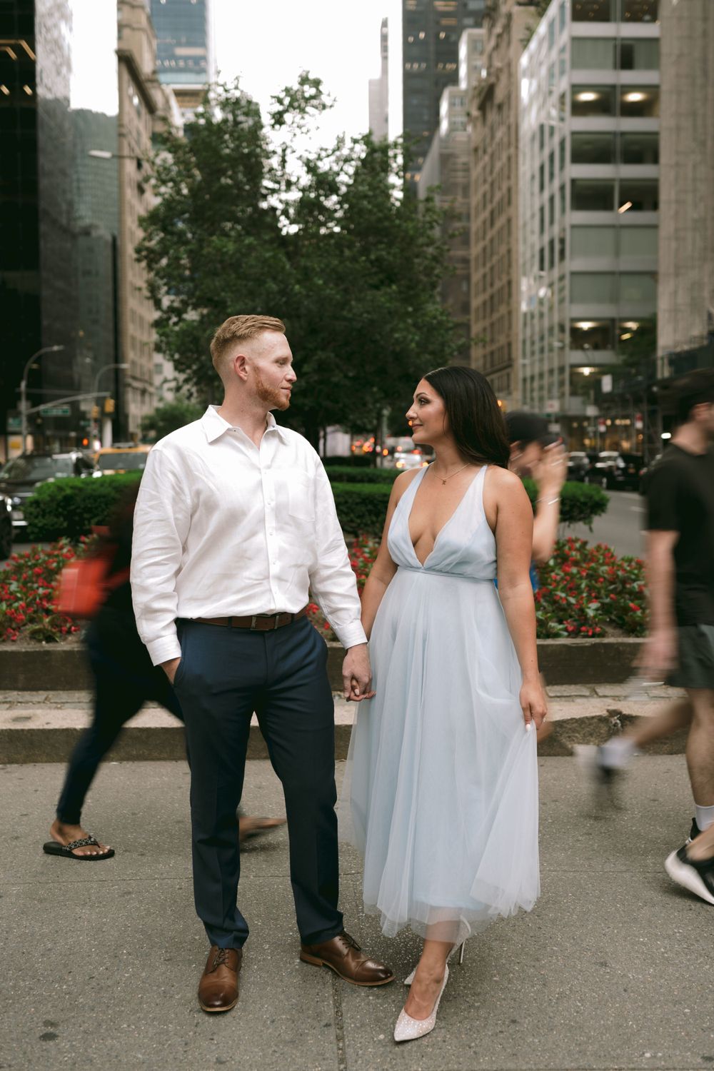 Engaged couple holds hands on a busy New York City street, woman wearing a light blue tulle dress.