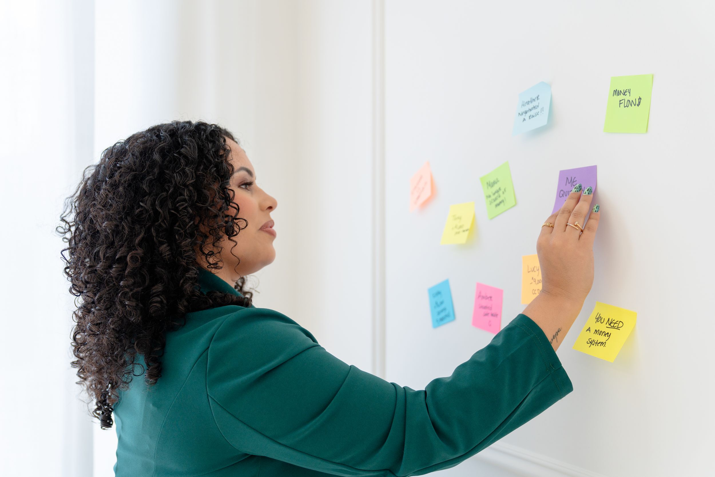 Person in green sweater placing colorful sticky notes on a white wall during a brainstorming session.