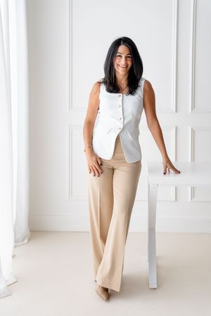 Stylish white sleeveless blouse paired with beige wide-leg trousers create a minimalist professional look against white backdrop.