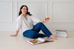 A person in blue jeans and a white top sits casually on a white floor while reading a book.