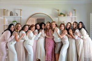 A row of bridesmaids in blush pink and white dresses pose together for a wedding party photo.