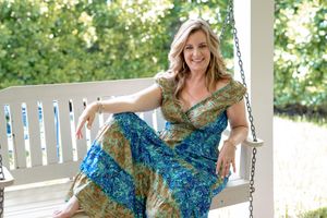 Someone relaxes on a white porch swing wearing a flowing blue and green patterned maxi dress in a sunny garden setting.