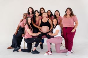 A group poses together in pink and dark clothing, highlighting togetherness and support around a pregnant figure.