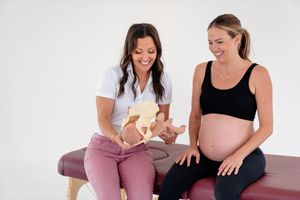 Healthcare provider reviews patient records while discussing pregnancy care during a medical consultation on an exam table.
