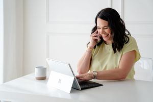 Two people sit at a desk with laptops, smiling and collaborating in a bright modern office space.