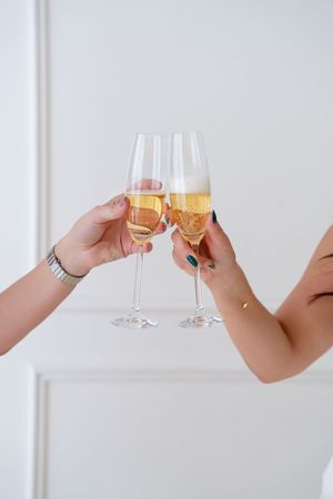 Multiple hands holding champagne glasses in a toasting gesture against a white background.