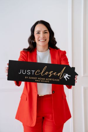 Professional in a bright red suit holds up pieces of a black sign with gold text in a clean white studio setting.