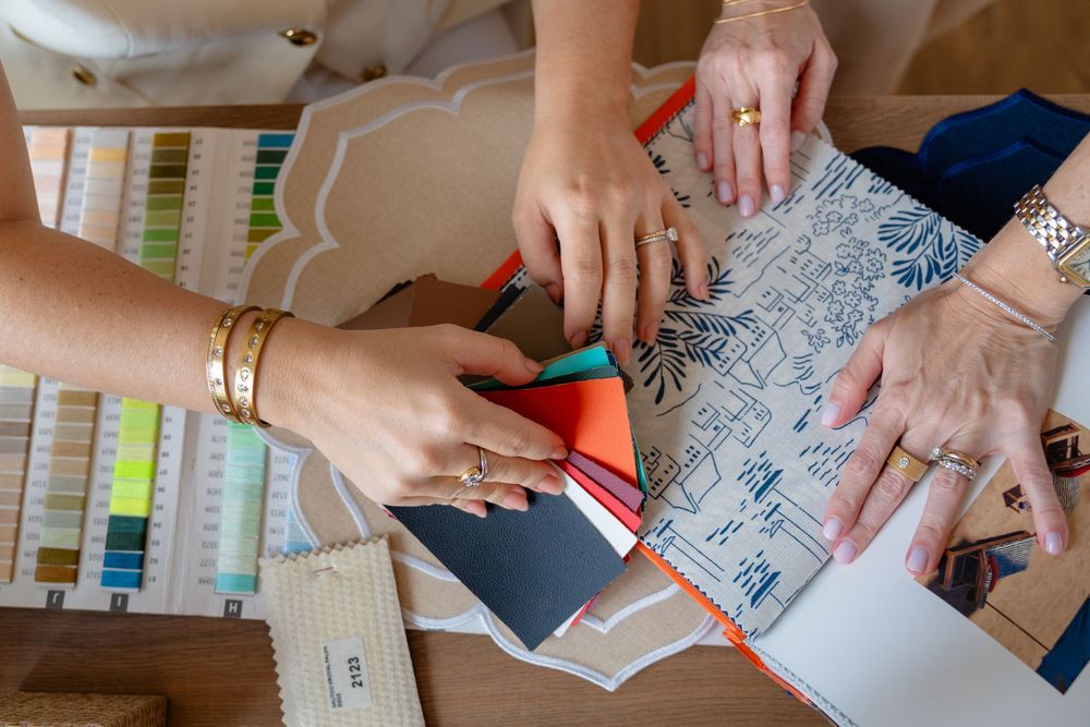 Two designers collaborate over fabric swatches and pattern samples on a wooden table in a design studio.