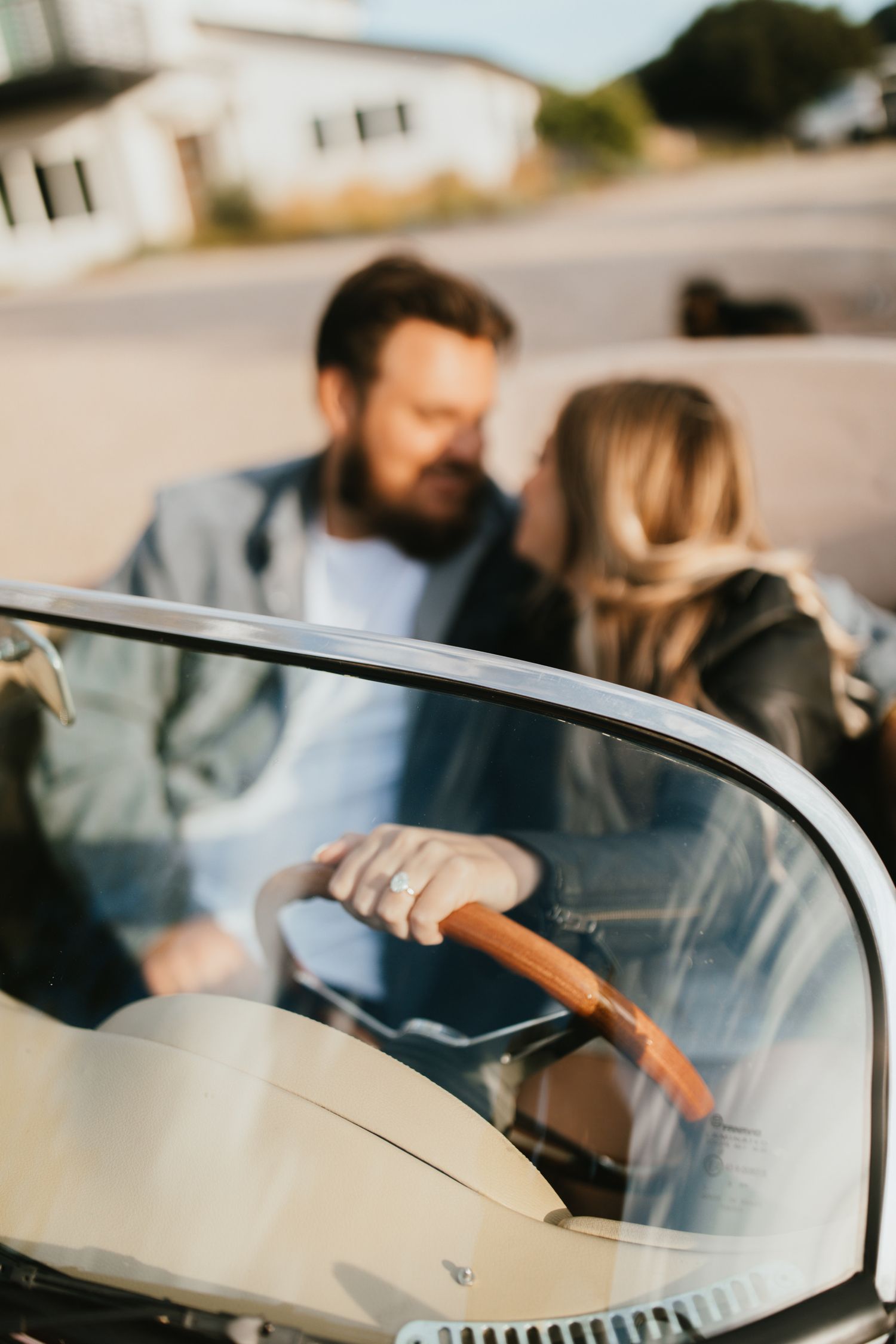 Close-up of hands on steering wheel with couple visible in background.
