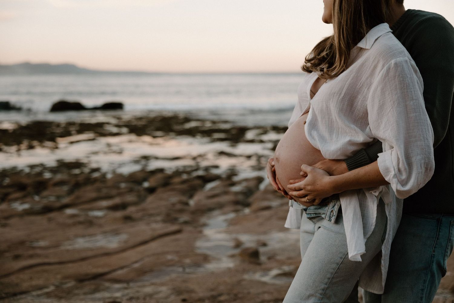 Close-up of baby bump with husband’s hands during a sunset maternity shoot in Bulli - maternity photography in Woonona and the Illawarra.