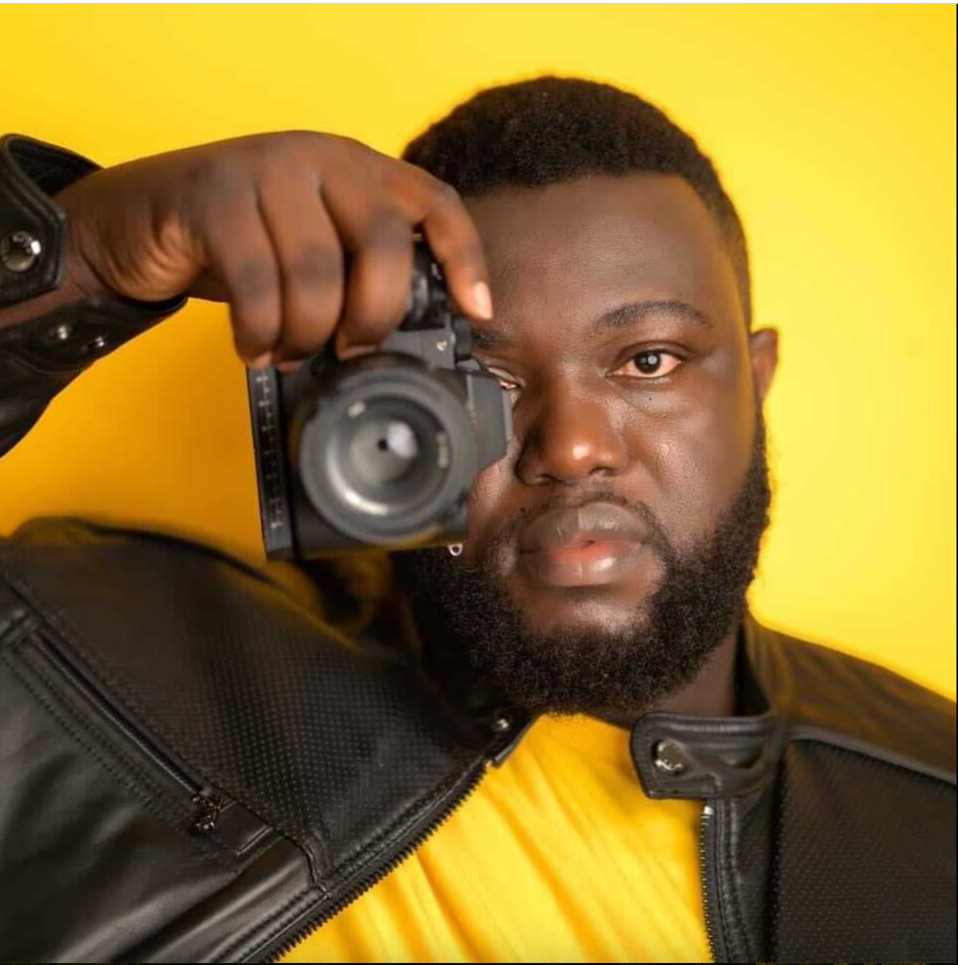 Professional photographer holds camera against vibrant yellow background.