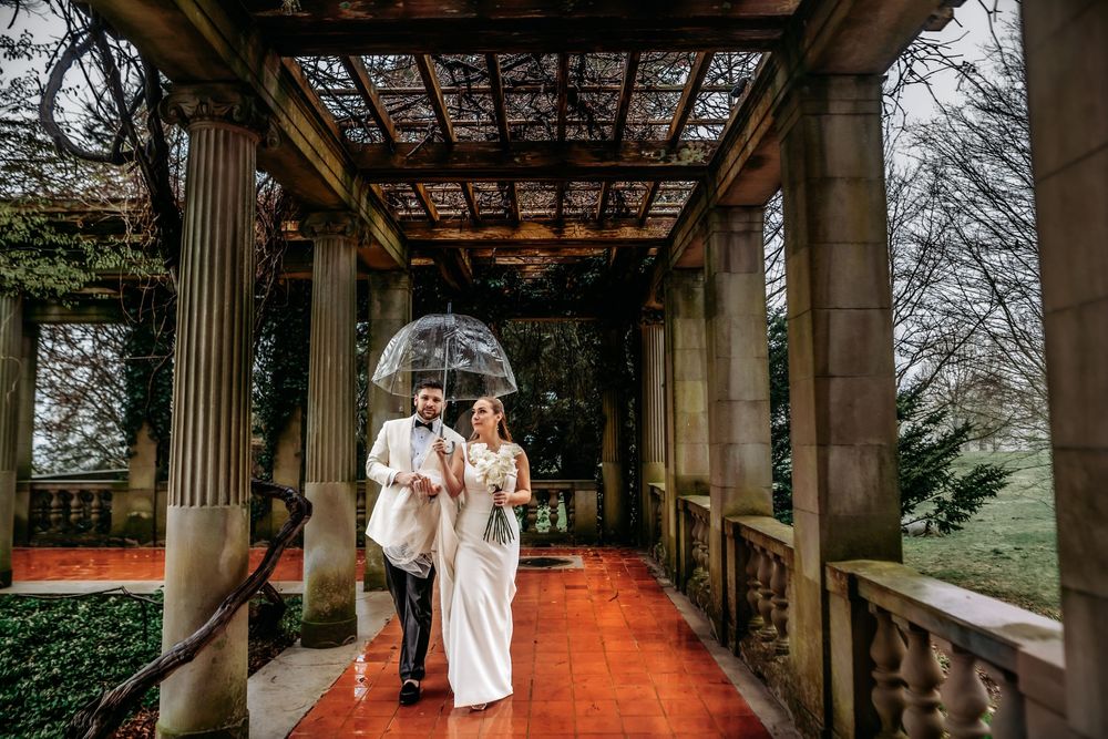 Couple shares an intimate moment under a covered stone walkway with columns during a rainy day.