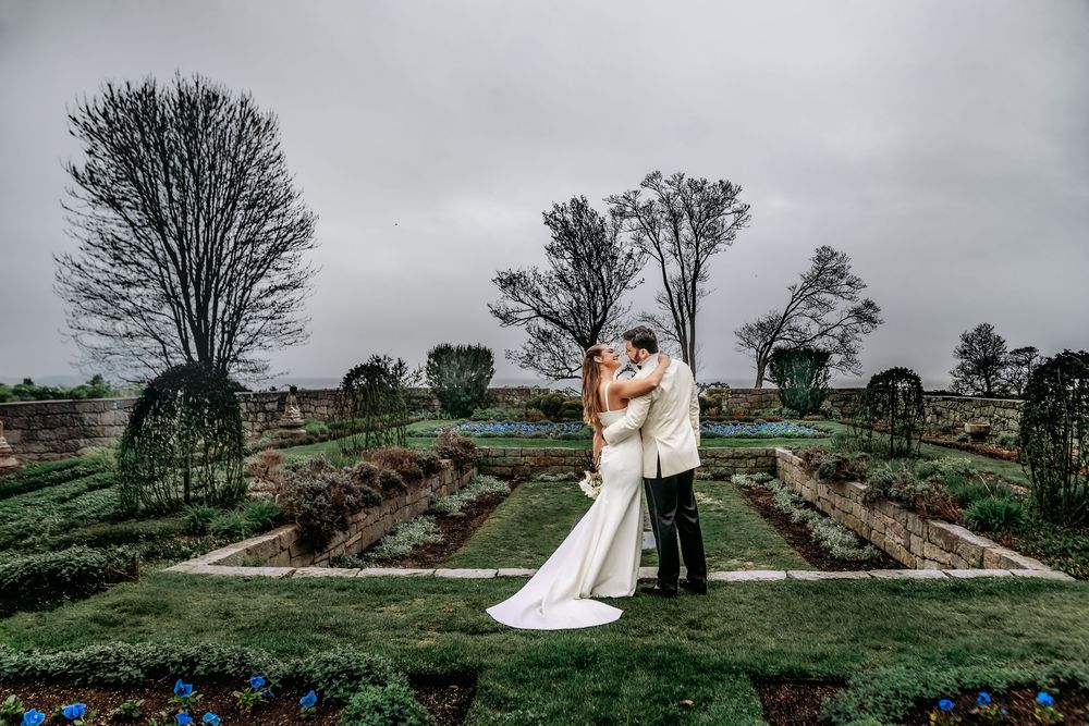 Romantic couple embraces on a scenic hilltop overlooking lush green landscapes during a cloudy wedding day.