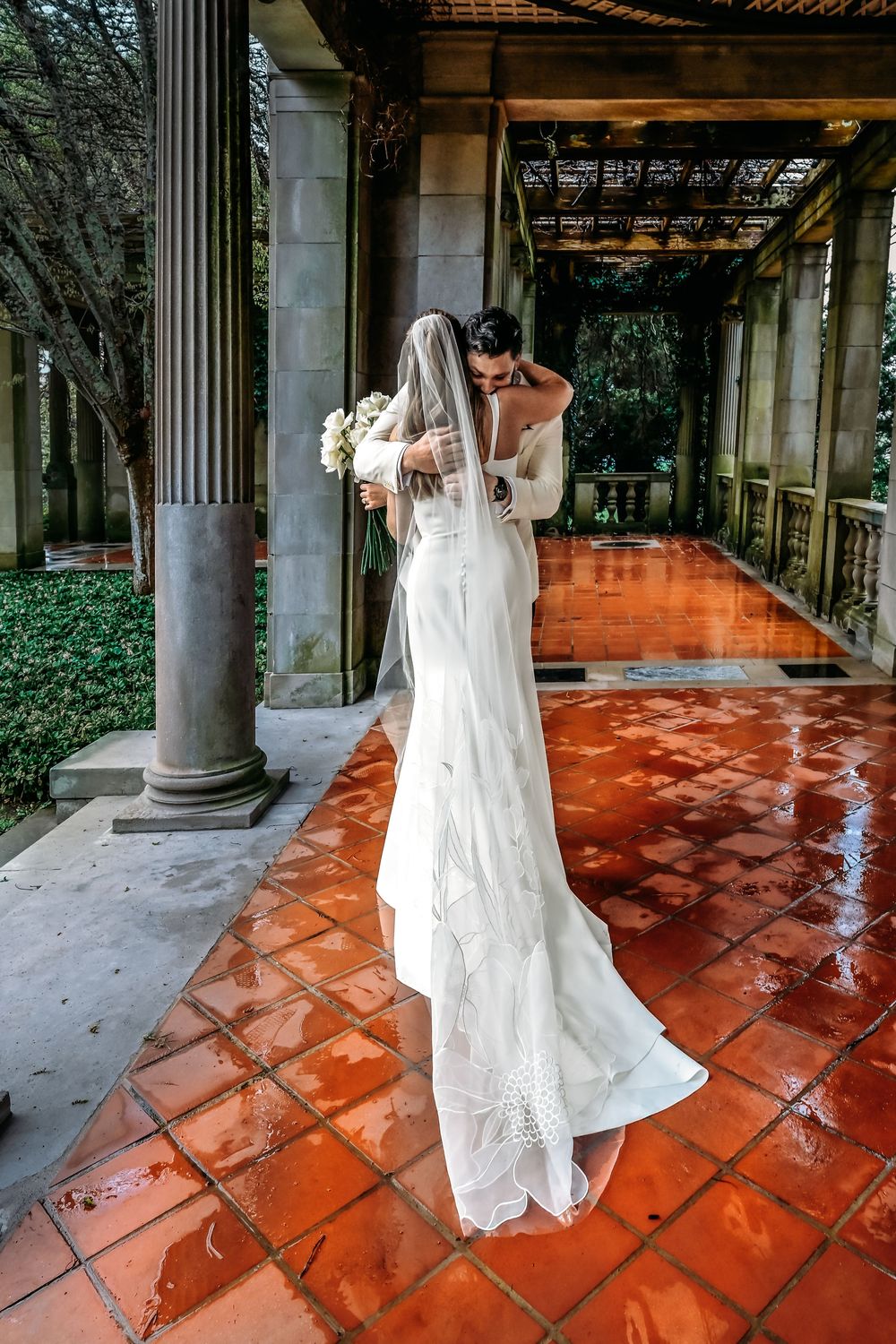 A wedding dress spins gracefully across a terracotta-tiled patio with classical stone columns and ivy-covered walls.