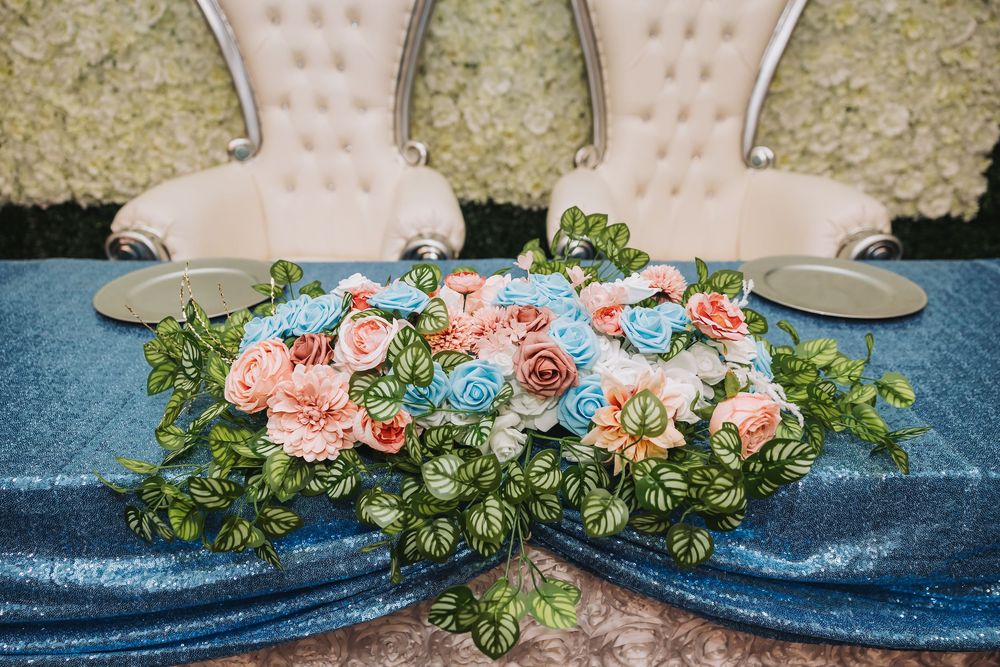 Wedding shoes displayed with delicate pink and blue floral arrangements on a blue velvet surface.