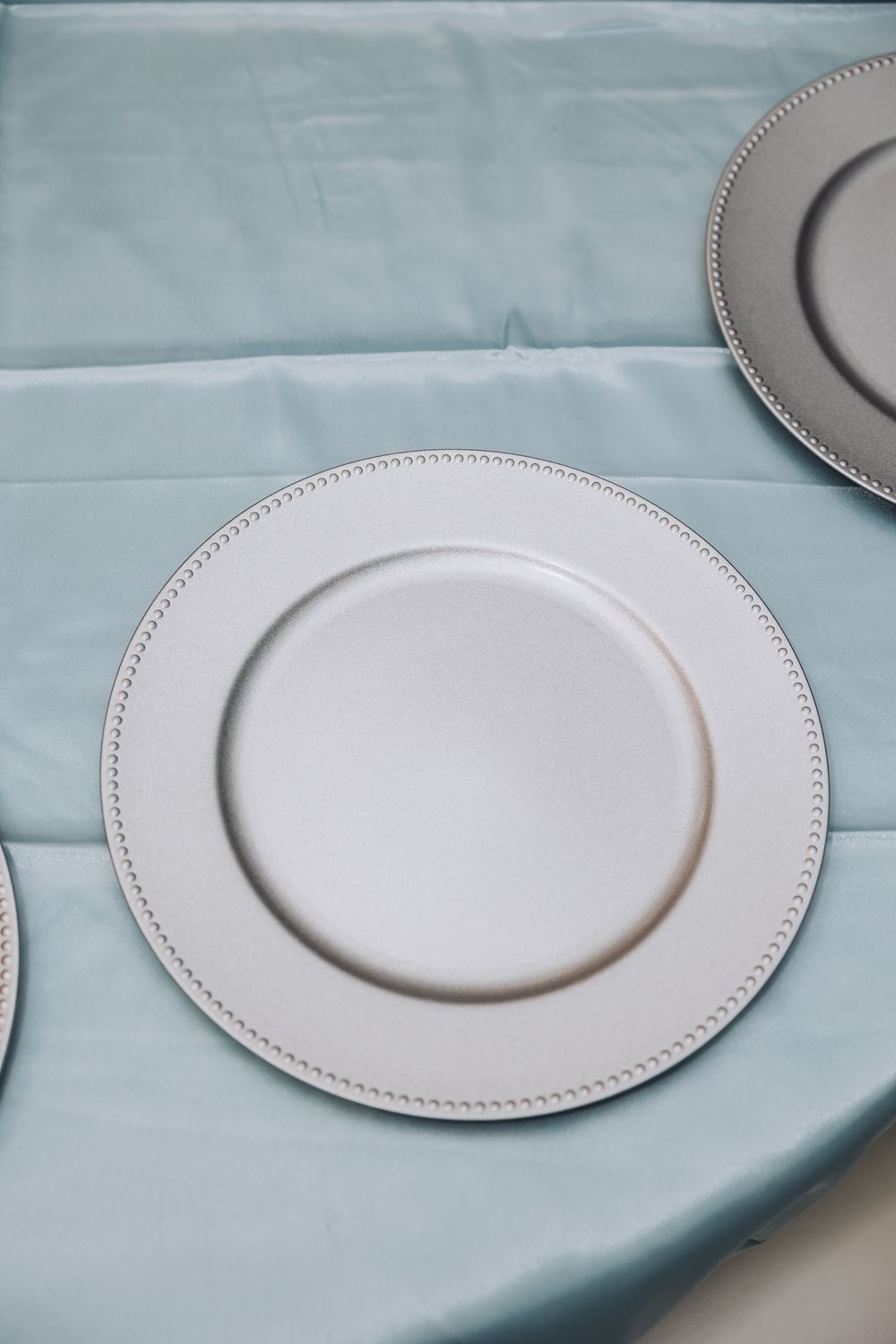 White decorative dinner plates with beaded trim edges arranged in a row on a light blue tablecloth.